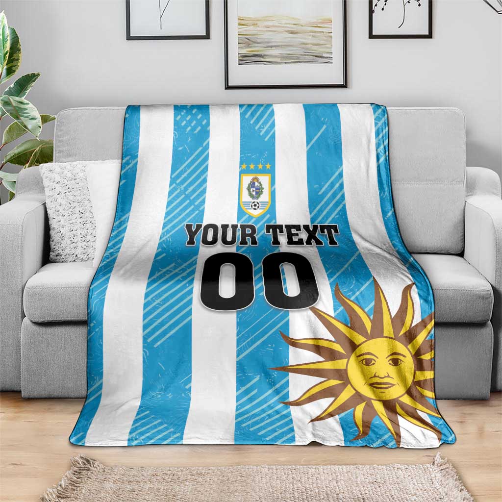 Blue and white striped football blanket with Uruguay crest, sun graphic, and 'YOUR TEXT 00'.