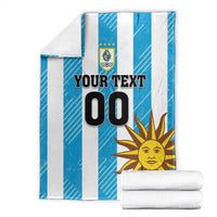 Stacked blue and white striped football blanket with Uruguay crest, sun graphic, and 'YOUR TEXT 00'.