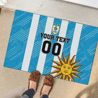 Blue rubber doormat with white stripes, 'YOUR TEXT 00', Uruguay crest and sun artwork.