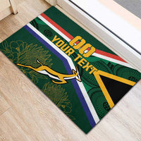Green rubber doormat on wood floor with South Africa flag pattern, 'DO' and 'YOUR TEXT'.
