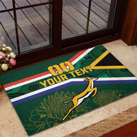 Green rubber doormat by doorway with South Africa stripes, stag mascot, and 'YOUR TEXT'.