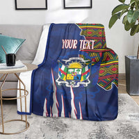 Personalized blue blanket laid over sofa seating, coat of arms design and kente border