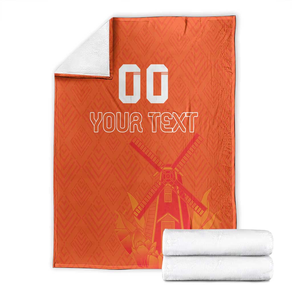 Orange rugby blanket folded with white towels, windmill and tulip pattern, 'YOUR TEXT' and '00'