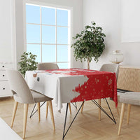 Red and white Christmas tablecloth draped on dining table with Santa and tree motifs
