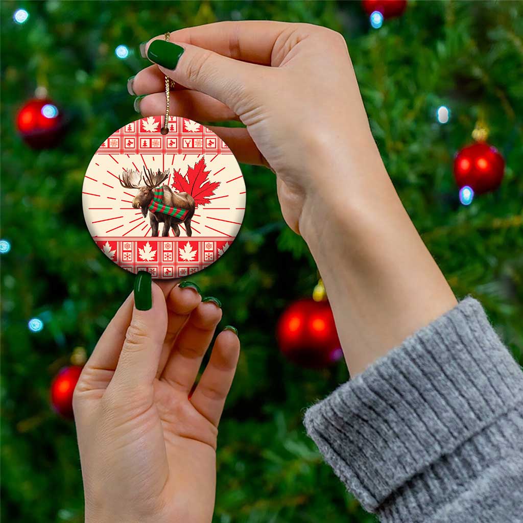 Round ceramic moose ornament with red maple leaf print, held by hand from gold string