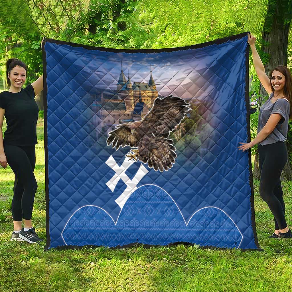 Blue quilt spread on grass featuring castle image, flying eagle, and white cross symbols