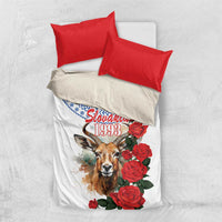 White bedding set on light background with red pillowcases, blue trim, chamois and red rose print
