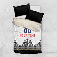 White bedding set laid flat: blue crest with '00', red 'YOUR TEXT', black Nordic pattern and trim