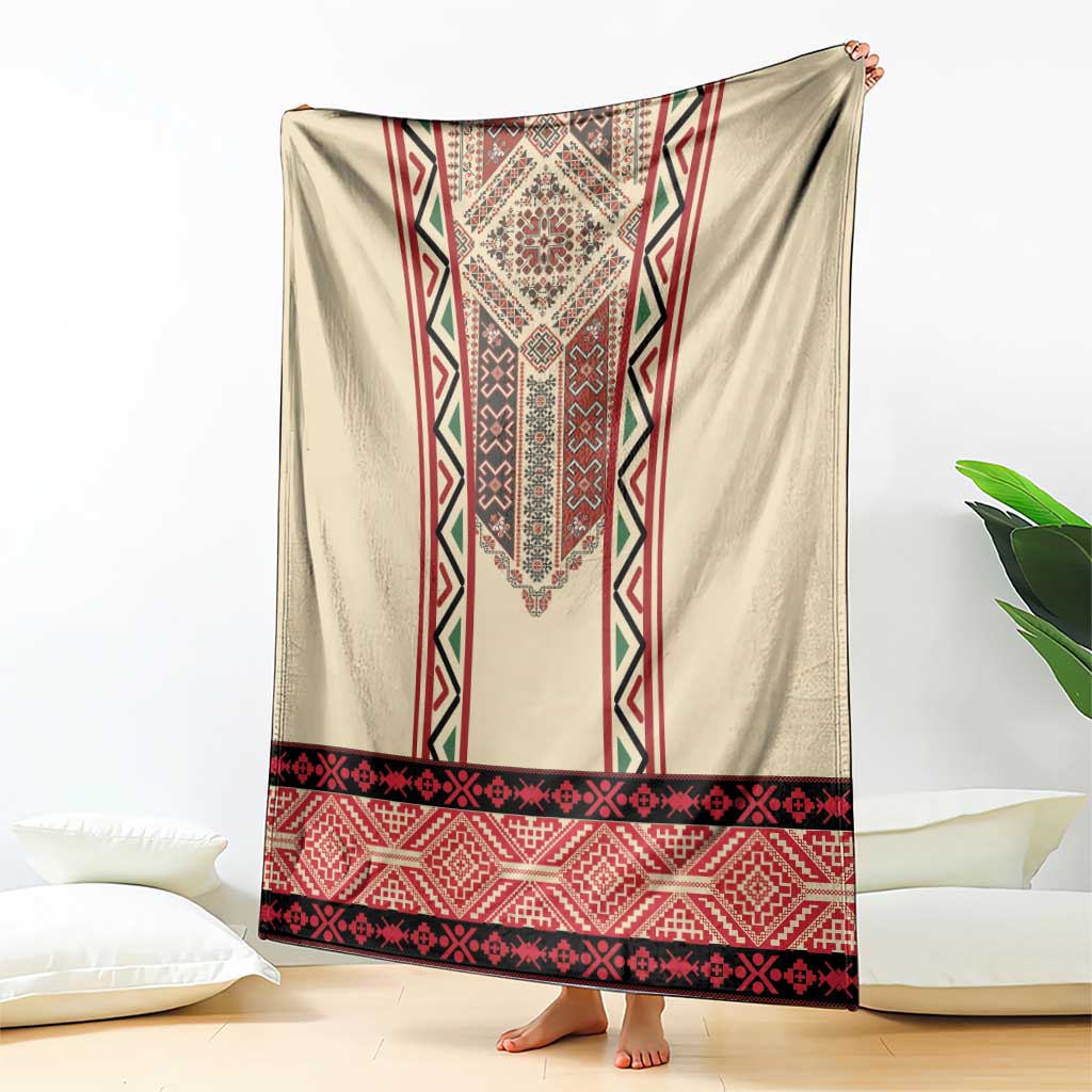 Beige blanket draped with red, black, green embroidery panel and border banding.
