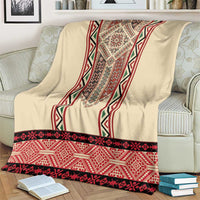 Beige blanket with red, black, and green embroidered vertical band and zigzag hem.