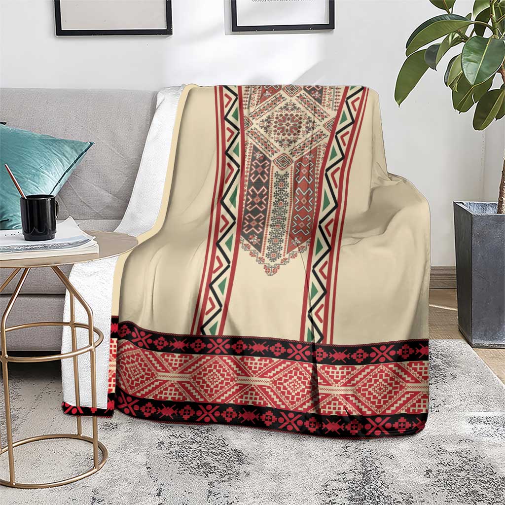 Beige blanket with red, black, and green embroidery stripe center and wide patterned hem.