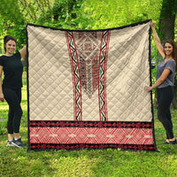 Beige quilt held outdoors, featuring red and black border and vertical embroidered motif.