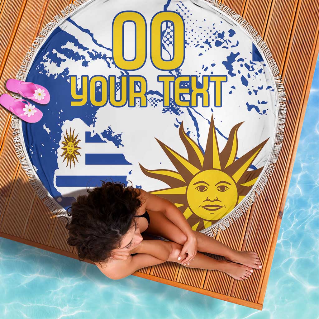Round blue-and-white beach blanket featuring Uruguay flag, sun face graphic, fringe edge
