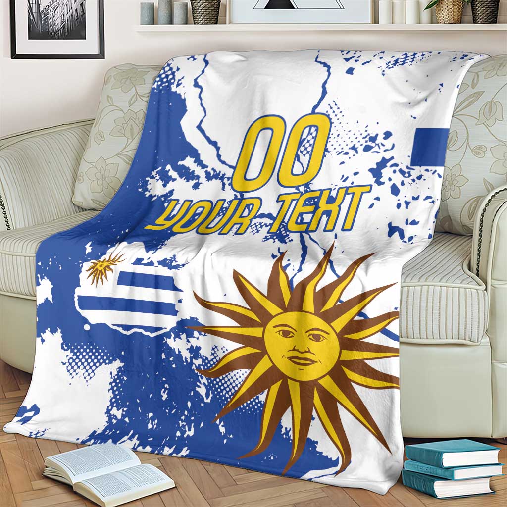 Blue and white Uruguay-themed fleece blanket with map splatter print, sun face, and “00 YOUR TEXT”