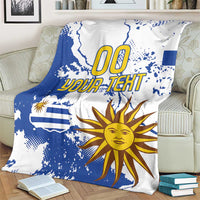 Blue and white Uruguay-themed fleece blanket with map splatter print, sun face, and “00 YOUR TEXT”