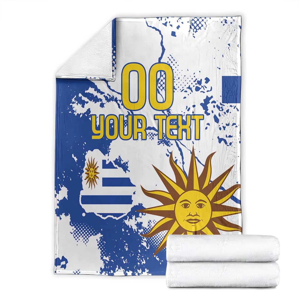 Folded blue and white Uruguay-themed blanket with sun face and “00 YOUR TEXT” lettering
