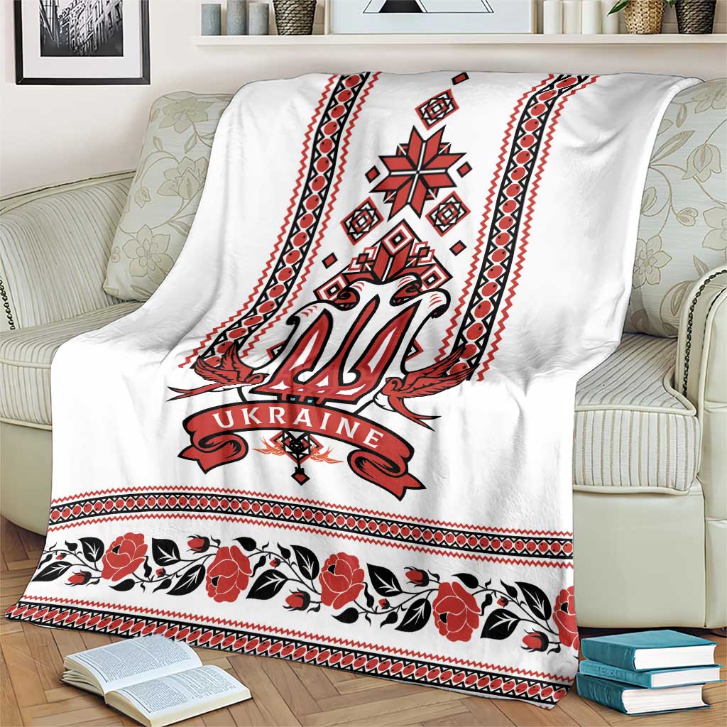 White blanket featuring red trident emblem, folk stripes, and floral band along the bottom