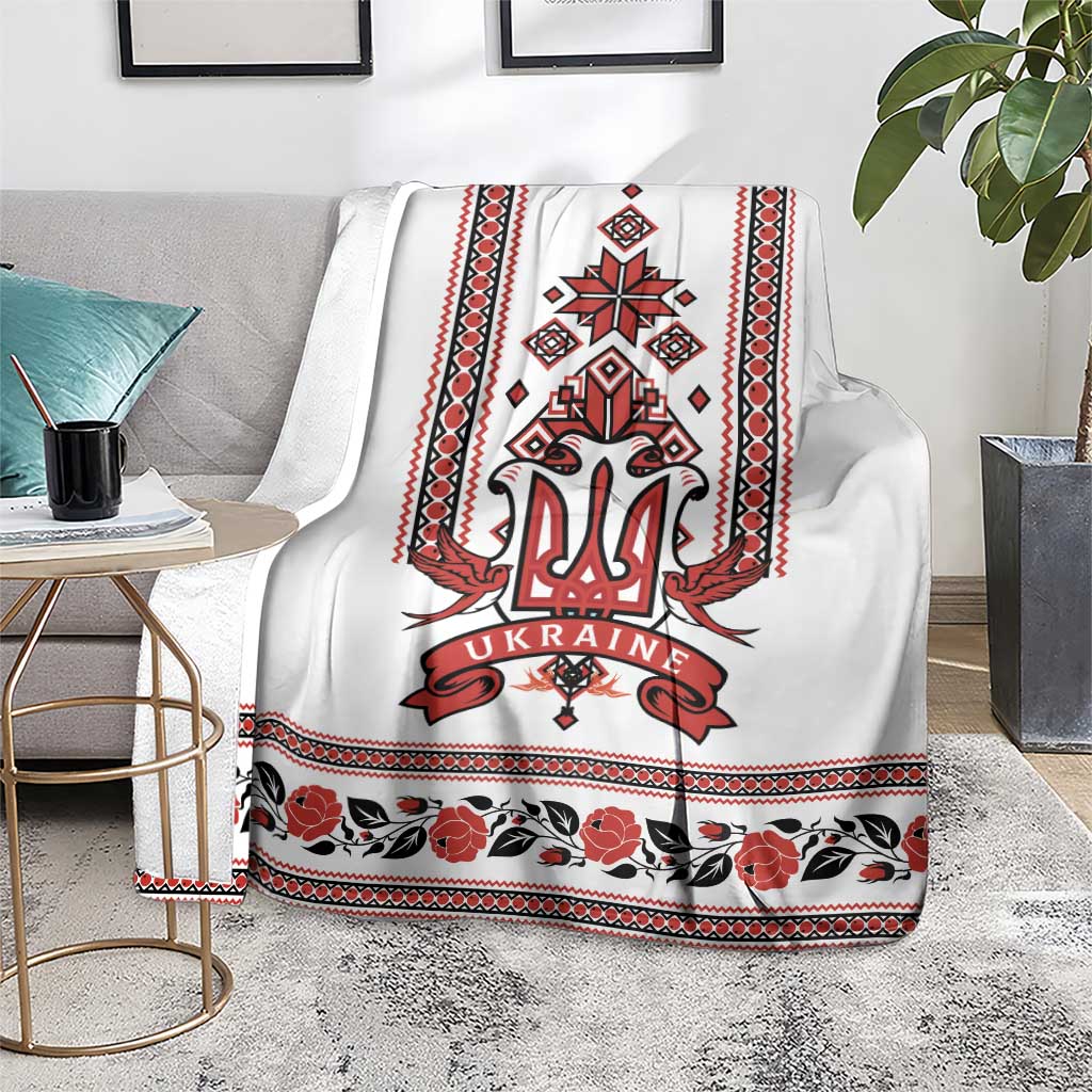 White trident folk blanket with red emblem, striped border, and dark floral row at hem