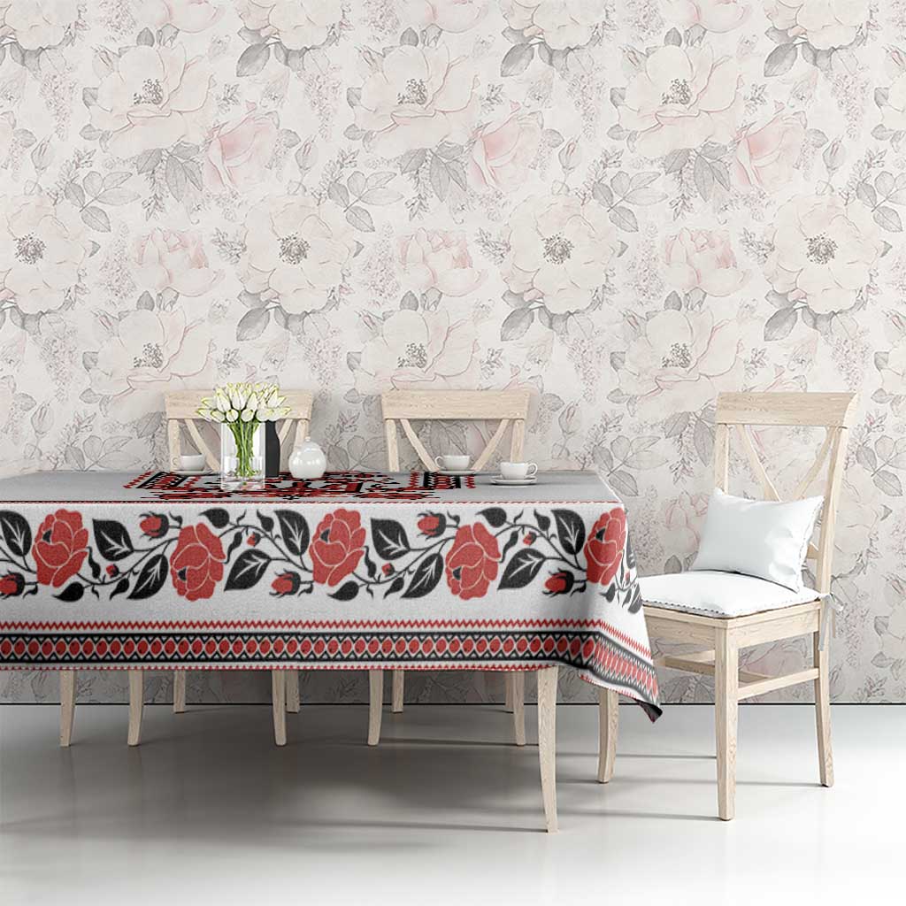 White tablecloth with red and black folk border and floral print over long dining table