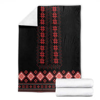 Black folk pattern blanket with red geometric motifs, with folded white towels
