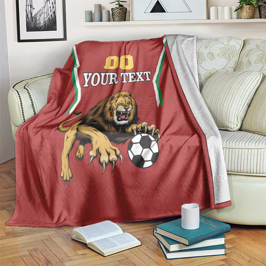 Red football blanket draped on sofa with lion and soccer ball, green trim, 00 'YOUR TEXT'
