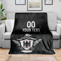 Black rugby blanket with eagle crest and '00 YOUR TEXT' print, laid on couch