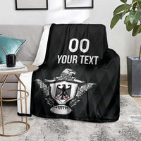 Black rugby blanket with eagle crest and '00 YOUR TEXT' print, on gray floor