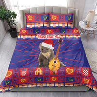 Christmas bedding set on a bed: blue and red plaid duvet and two pillowcases with “Merry Christmas” and cat