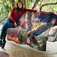 Quilt draped on couch, quilted diamond pattern with Serbia eagle, crest patch, multicolor backdrop.
