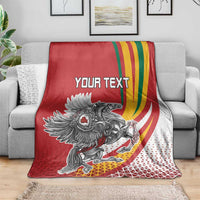 Red personalized throw blanket on gray couch, crest graphic, rainbow swoosh, 'YOUR TEXT' text