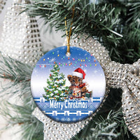Blue round ceramic Christmas ornament hanging on a tree, cat Santa hat and “Merry Christmas”