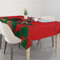 Red tablecloth with green geometric motif and rooster graphic across the table surface.