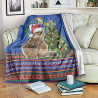 Blue Christmas blanket with cat in red hat, evergreen tree, and colorful folk stripe border