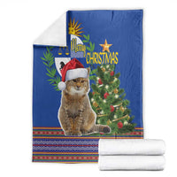 Blue Christmas blanket with cat in red Santa hat and evergreen tree, with folded white blankets