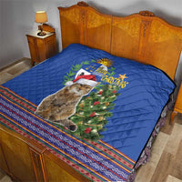 Blue Christmas quilt on bed with pampas cat, green tree, and multicolor folk striped border.