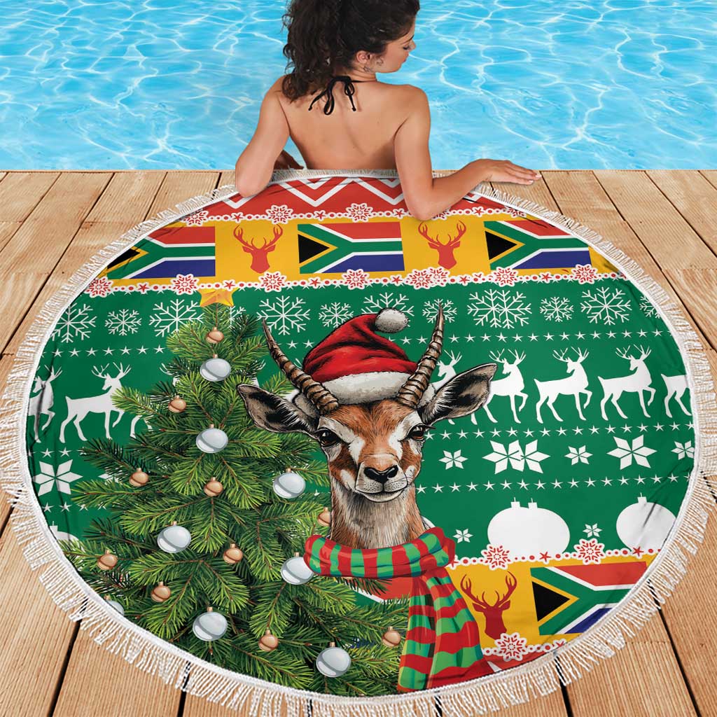 Round Christmas beach blanket showing springbok with red hat, pine tree, baubles, and fringe