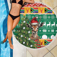 Close-up of round Christmas beach blanket with springbok, pine tree, baubles, and white fringe