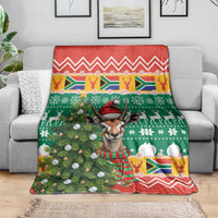 Christmas blanket spread on sofa, springbok wearing Santa hat amid pine tree and snow motifs
