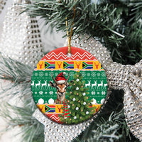 Round ceramic Christmas ornament hanging on a tree branch; springbok in hat on green pattern