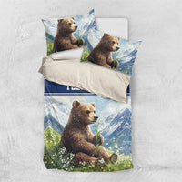 Folded blue bedding set with brown bear, mountains, garden flowers, and blue “YOUR TEXT” strip.