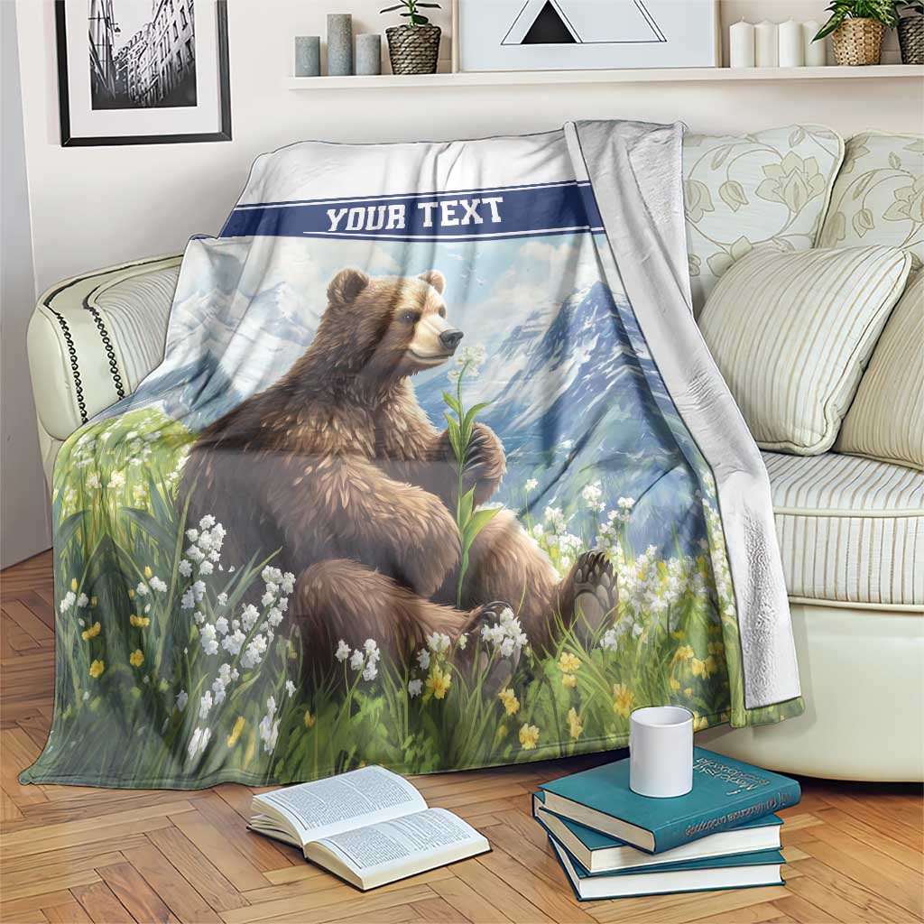 Personalized throw blanket with brown bear, flowers, mountains and 'YOUR TEXT' blue banner