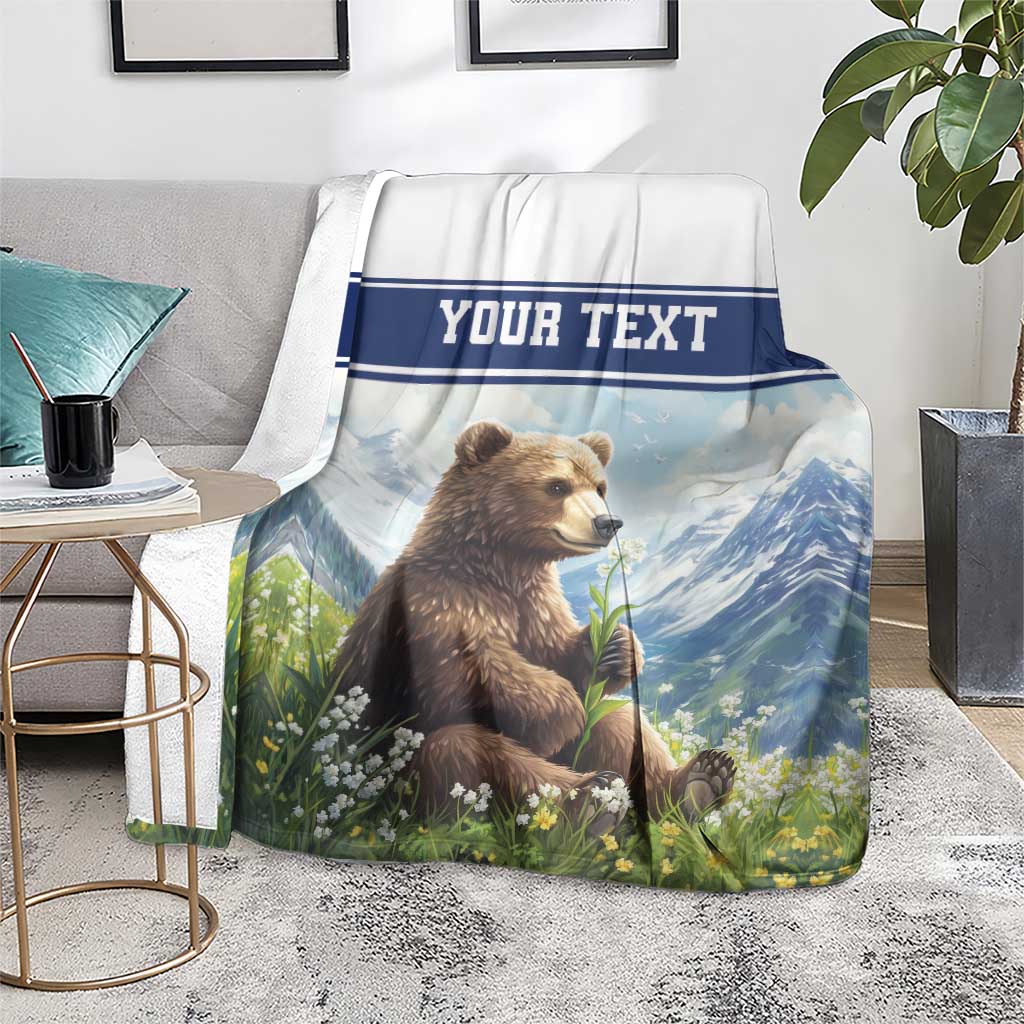 Personalized throw blanket on floor with brown bear in flowers, blue mountain scene, 'YOUR TEXT'