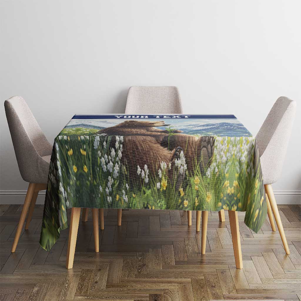 Personalized tablecloth with blue border, bear in green meadow, on dining table