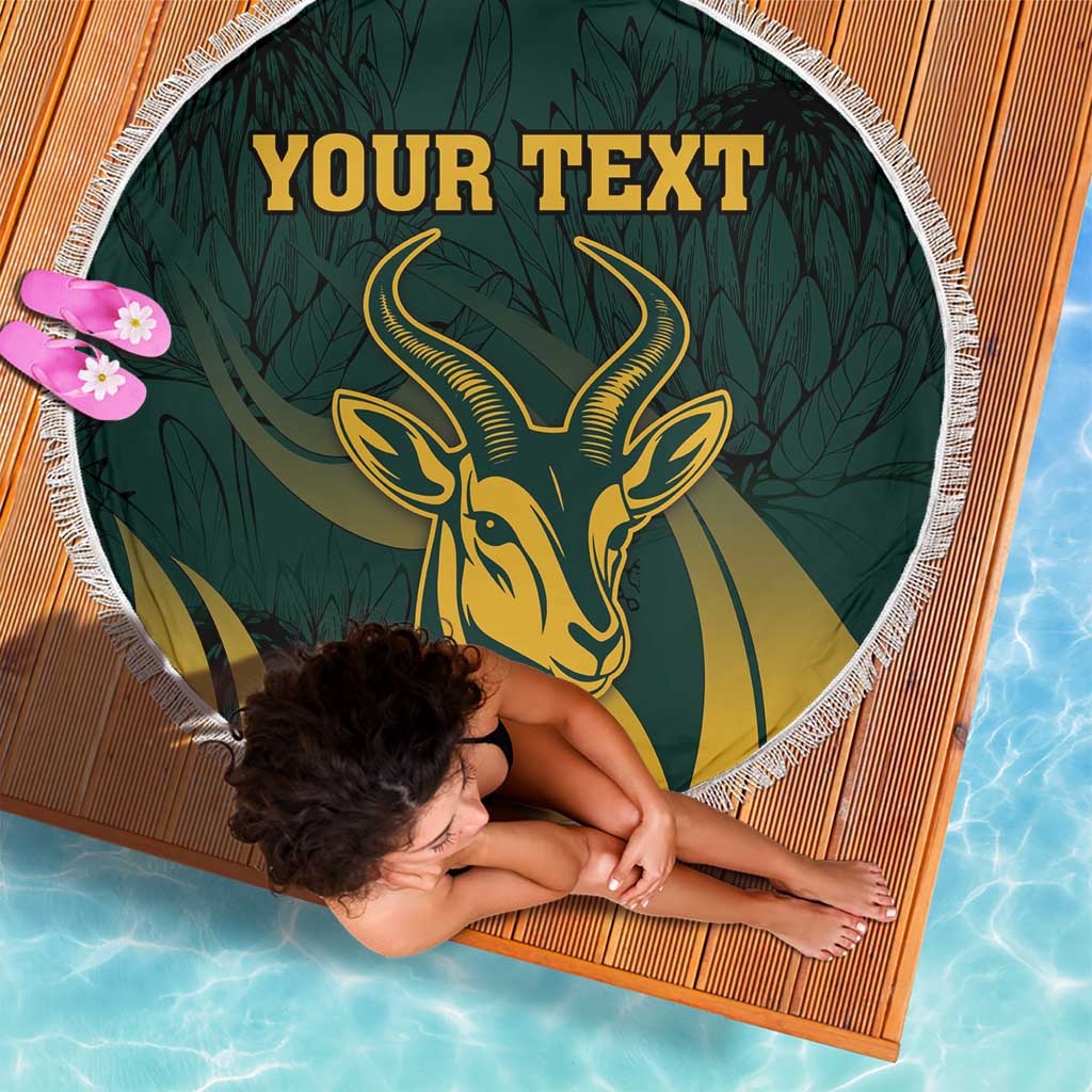 Green round beach blanket with fringe edge, gold springbok emblem and leafy pattern, custom text