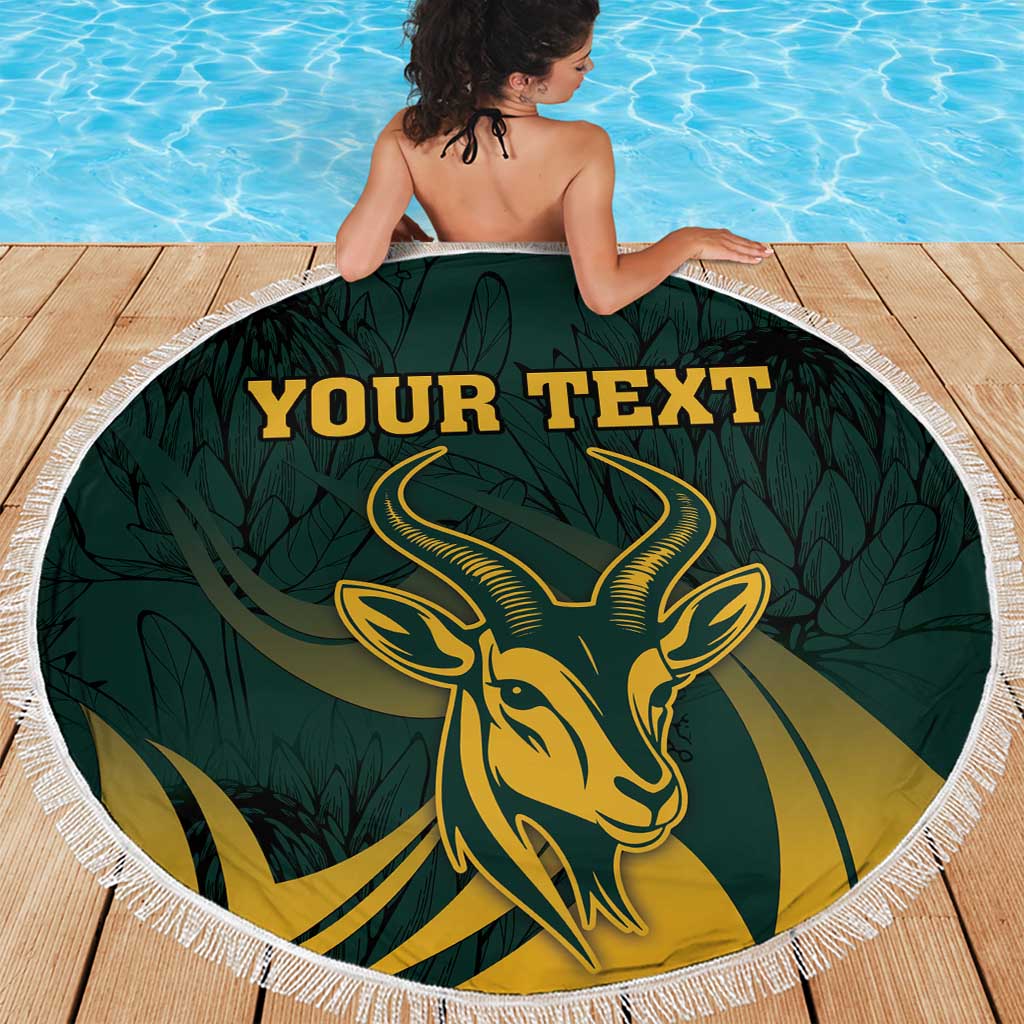 Green round beach blanket with fringe edge, gold springbok emblem filling center, custom text