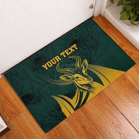 Green rubber doormat on wood floor with golden springbok graphic and 'YOUR TEXT' text