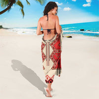 Beige sarong with red, black, and white geometric motifs, worn as a wrap
