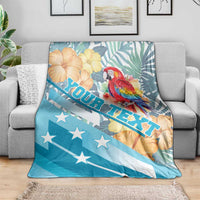 Personalized blue blanket with macaw, tropical leaves, flowers, and ROATAN text on couch