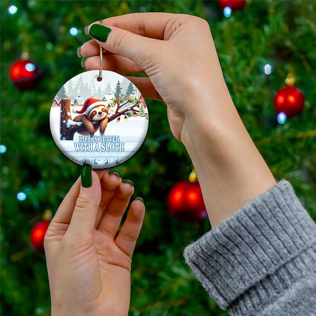 Blue ceramic round sloth ornament held in hand, snowy forest artwork with Santa hat.