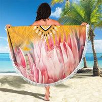 Round beach blanket with yellow-and-black emblem center, pink floral pattern, white fringe